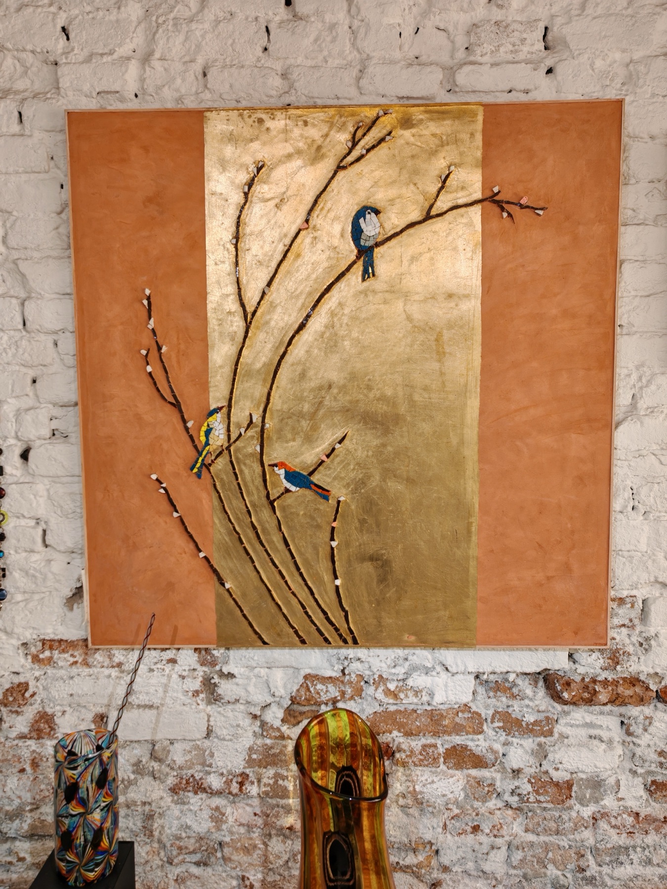 A mosaic artwork of birds on gold leaf above Murano glass vases