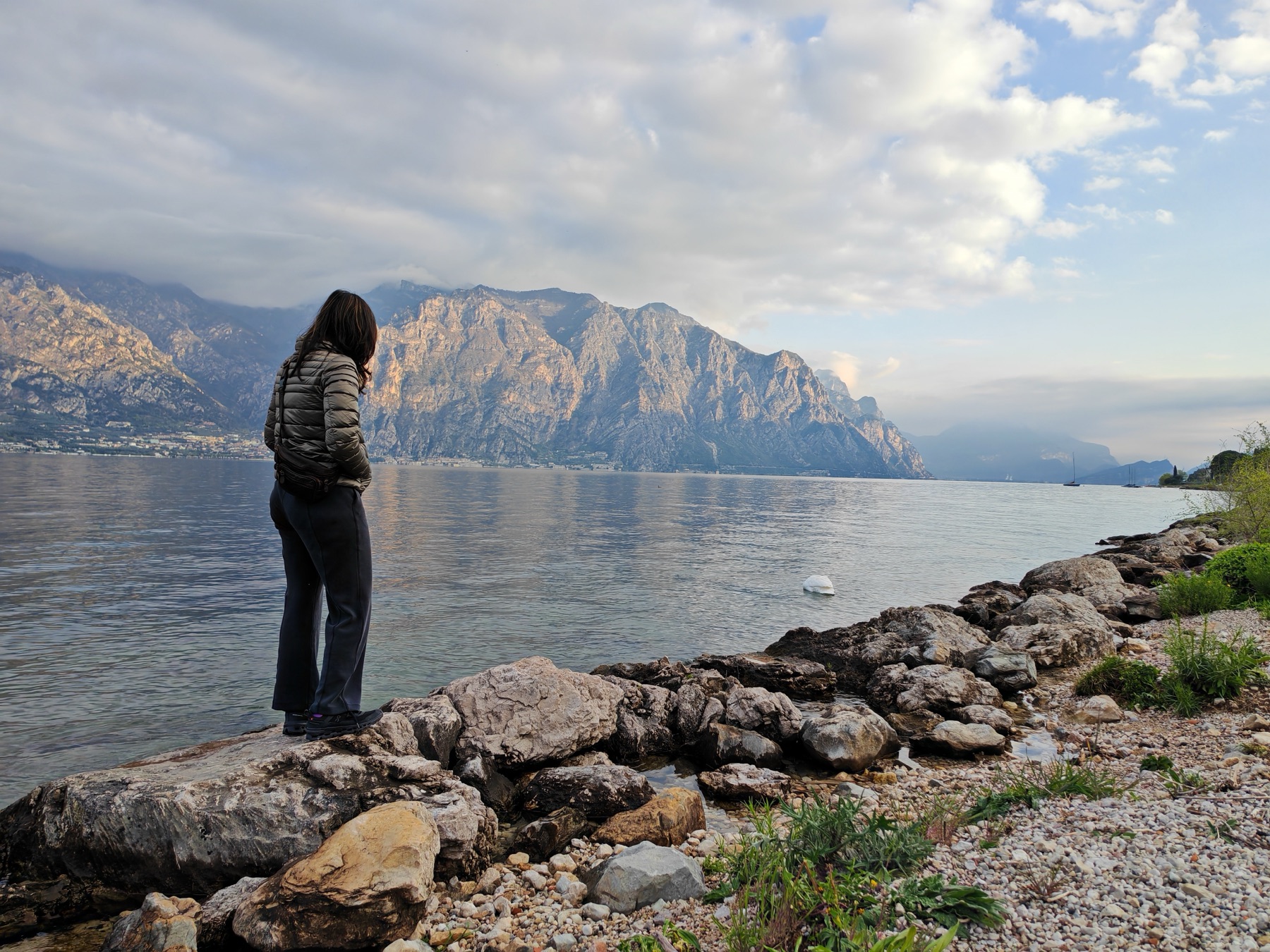 Pallavi standing on lakeside rocks, looking across Lake Garda at the mountains