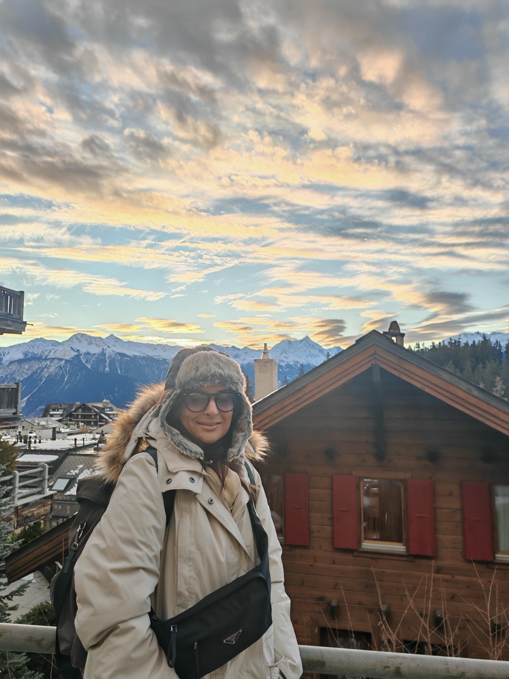 Pallavi at sunset in front of a wooden chalet and snowy peaks